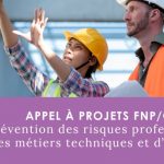 Une femme et un homme en équipements de chantier. La femme indique des manœuvres à son collègue qui lui tient des plans dans les mains.